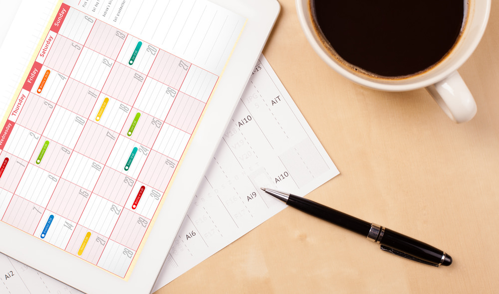 Tablet pc showing calendar on screen with a cup of coffee on a d